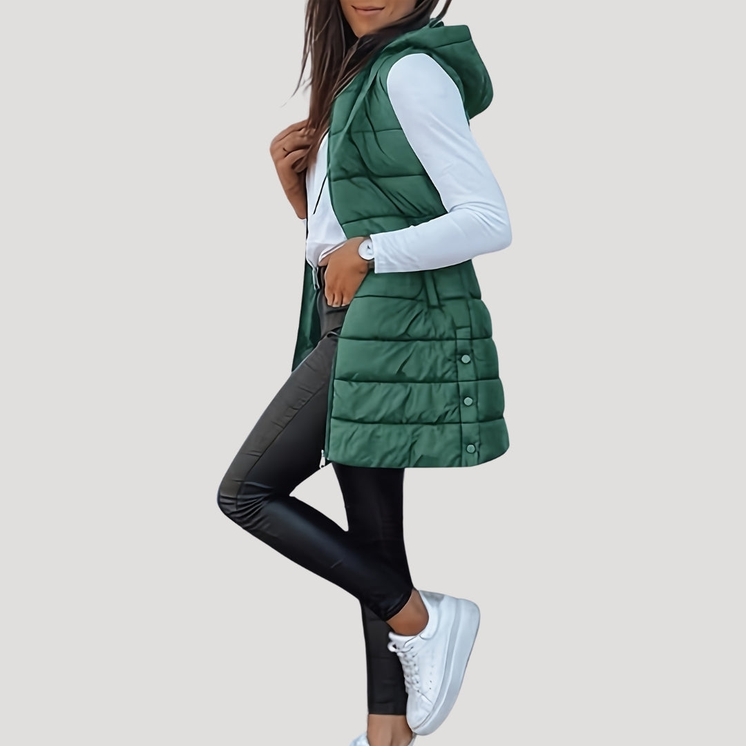 Woman wearing a forest-green hooded quilted vest over a white long-sleeve top, black faux-leather leggings and white sneakers